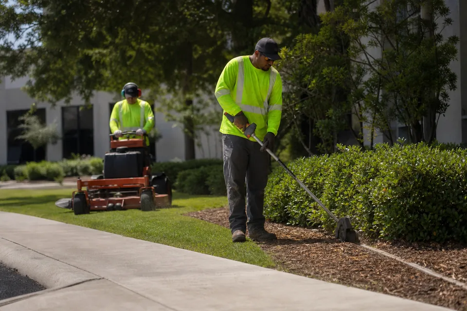 Two-person lawn crew mowing and edging a commercial property lawn on a weekly maintenance visit